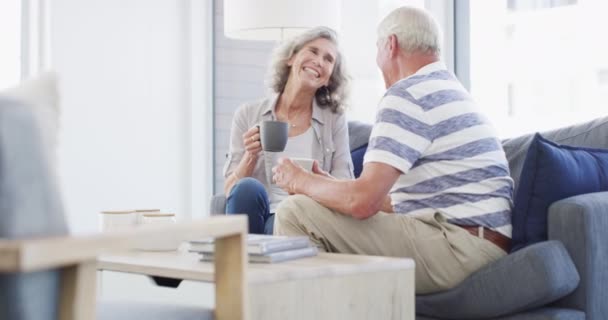 Lieben, entspannen und Senioren-Paar auf einem Sofa mit Kaffeepause Gespräch und Bindung, kostenlos oder Chillen zu Hause. Glückliche, unterstützende und alte Menschen im Wohnzimmer mit Kommunikation, Tee und genießen den Ruhestand. - Filmmaterial, Video