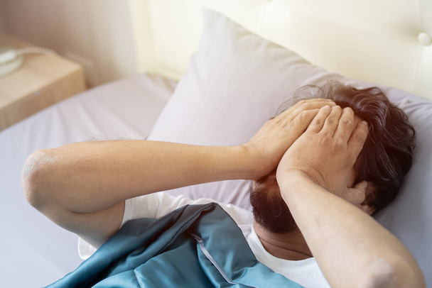 Тысячелетний мужчина трогает голову бессонницей и симптомом головной боли, лежа в постели в современной спальне. - Фото, изображение