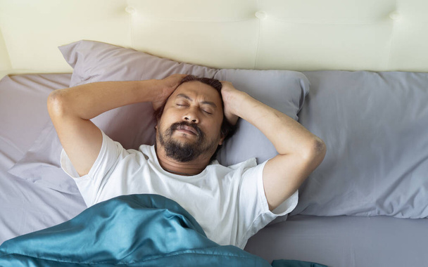 Schlafloser junger Mann, der allein im Bett liegt, seinen Kopf berührt, schwere Gedanken hat oder an Migräne leidet, Draufsicht, Kopierraum - Foto, Bild