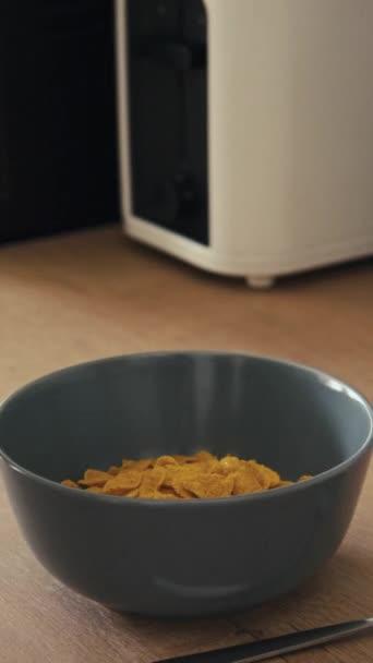Coltellata laterale verticale di latte versato a mano in una ciotola di cereali sana sul tavolo in legno nella cucina moderna - Filmati, video