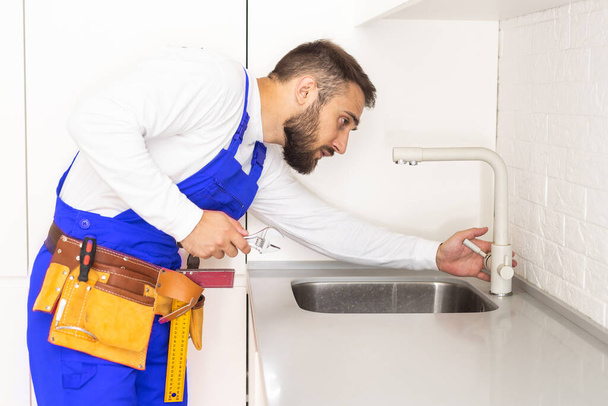 junger Reparateur installiert Wasserhahn der Spüle in der Küche. - Foto, Bild