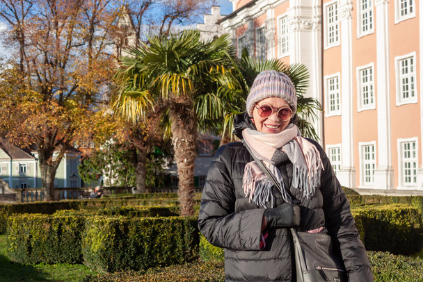 Портрет зрелой женщины в пиджаке, шляпе и солнцезащитных очках в парке возле замка в Меерсбурге - Фото, изображение