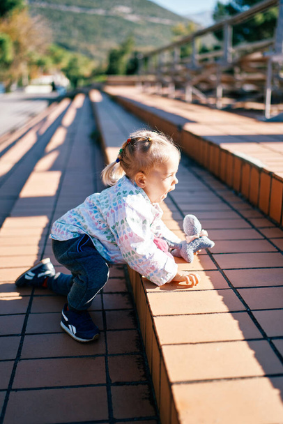 小さな女の子は,彼女の手にあるおもちゃで,すべての4つのコースで公園のステップを登ります. 高品質の写真 - 写真・画像
