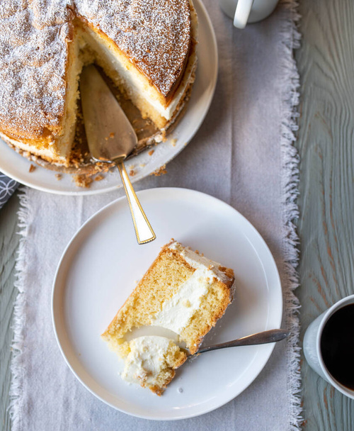 Traditional german cheese cream cake fresh and homemade baked. Served ready to eat on a table. Whole and a slice of cake with coffee. Table top view - Photo, Image