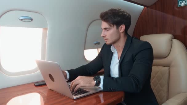 Komea mies tyylikkäässä puvussa työskentelee kannettavan tietokoneen lentäessään mukava lentokone työtä kannettavan symboli modernin ammattien menestyksekkään uran. Työ kannettavan tietokoneen taivaalla sekoittamalla vapautta onnea - Materiaali, video