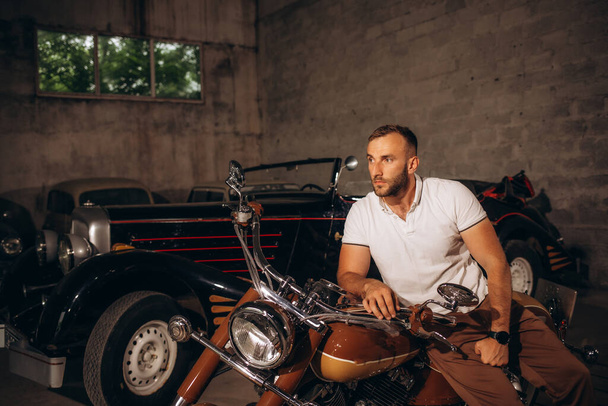 A man sits on a retro motorcycle in his garage - Photo, Image
