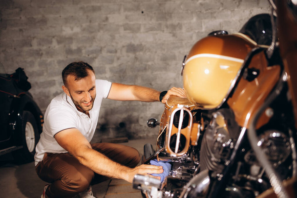 Egy férfi leporolja a retro motorját a garázsban. - Fotó, kép