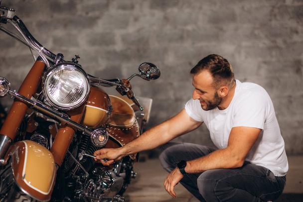 Ein Mann staubt sein Retro-Motorrad in der Garage ab - Foto, Bild