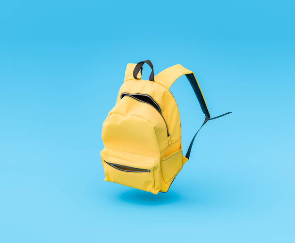 3D rendering of a vibrant yellow backpack suspended in the air on a solid blue background, concept of education and learning. - Photo, Image