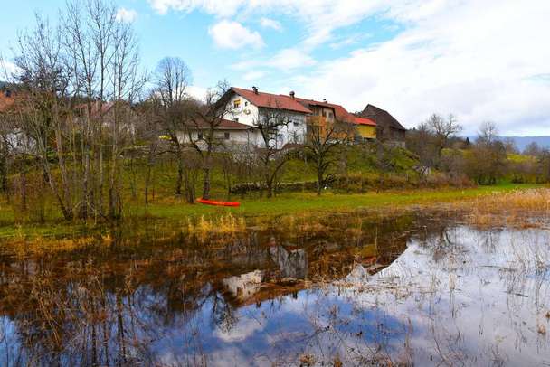 Pueblo de Laze pri Gorenjem Jezeru y un reflejo de los edificios en el lago Cerknisko jezero en Notranjska, Eslovenia - Foto, Imagen