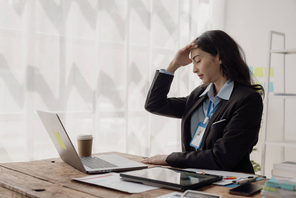 Unavená asijská obchodní žena ospalý a znuděný z sezení u stolu na dlouhou dobu a s kancelářským syndromem cítím bolest hlavy z pohledu na obrazovku příliš dlouho. - Fotografie, Obrázek