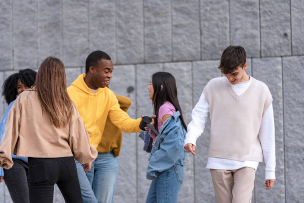 Groupe de jeunes amis s'engageant dans la danse et la conversation dans un contexte de béton gris, incarnant les loisirs urbains - Photo, image