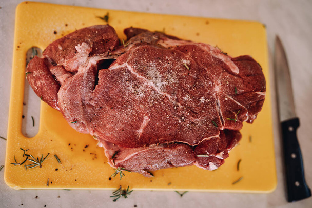 Сирий шматок м'яса, посипаний подрібненим розмарином, спеціями та сіллю, лежить на обробній дошці. Високоякісна фотографія - Фото, зображення