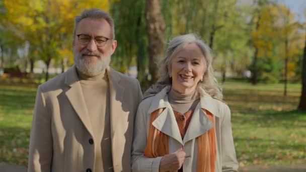 Portré boldog érett pár mosolyog ősszel park vidám öregasszony férfi pózol együtt kamera a természetben szabadban elegáns idősebb férj feleség nyugdíjas család nevetés szórakozás szerelem kapcsolat - Felvétel, videó