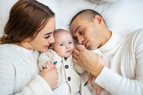 Above, portrait and happy parents with baby on bed for love, care and quality time together at home. Smile of mother, father and family with cute newborn kid relax in bedroom, support and happiness. - Photo, Image