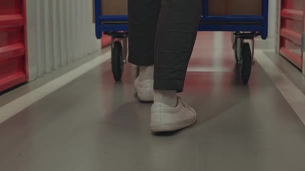 Gekippte Rückansicht des Mieters zu Fuß durch Self-Storage-Korridor mit Dolly-Wagen mit Kartons beladen - Filmmaterial, Video