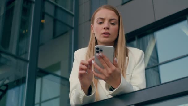 Ευγενικός Καυκάσιος γυναίκα επιχειρηματίας γυναίκα επιχειρηματίας επιχειρηματίας γυναίκα υπάλληλος κρατώντας τηλέφωνο σκέψης κοντά στο εταιρικό κτίριο γραφείων καταλήξει σε σχέδιο χρησιμοποιώντας το smartphone σκεφτείτε αναλογιστείτε ιδέα - Πλάνα, βίντεο