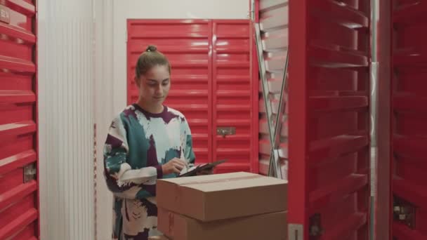 Jovem mulher usando tablet digital e falando com o marido passando enquanto traz caixas com seus pertences para a unidade de armazenamento de auto - Filmagem, Vídeo