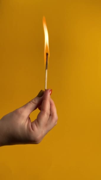 Eine unkenntliche weibliche Person hält ein brennendes Streichholz in der Hand, bläst die Flamme sanft aus und deckt den verblassenden Rauch isoliert auf orangefarbenem Hintergrund auf. Drinnen vertikale Studioaufnahmen. Abstraktes Konzept des Burnouts - Filmmaterial, Video