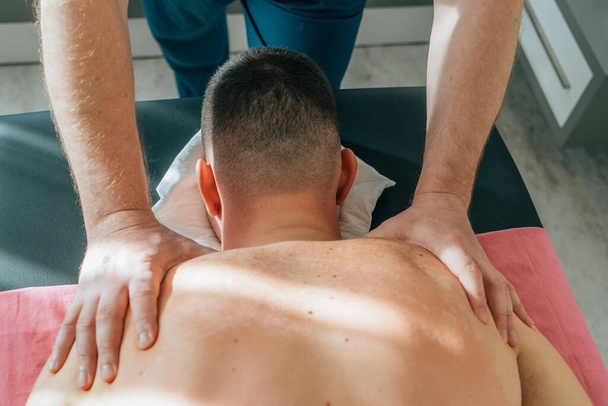 Masażysta masujący plecy młodego mężczyzny leżącego na stole do masażu. Masaż relaksacyjny i leczniczy. - Zdjęcie, obraz