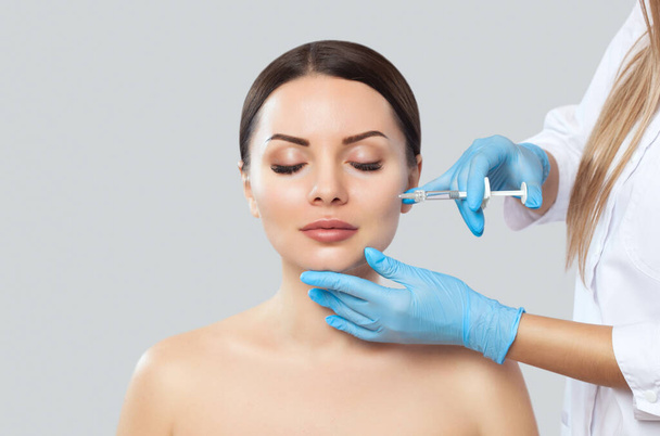 Doktor kozmetik uzmanı güzellik salonundaki güzel bir kadının cildindeki kırışıklıkları sıkmak ve düzleştirmek için canlandırıcı enjeksiyon prosedürü uyguluyor.. - Fotoğraf, Görsel