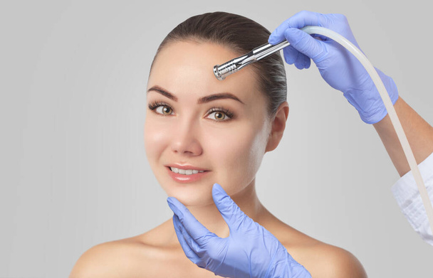 There is a woman, who is making the procedure Microdermabrasion of the facial skin in a beauty salon.Cosmetology and professional skin care. - Photo, Image
