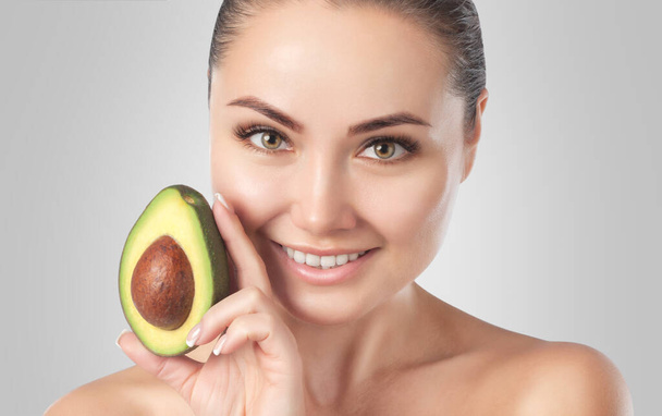 Mooie glimlachende vrouw met een schone huid houdt rijpe avocado in de buurt van het gezicht. Cosmetologie huidverzorging - Foto, afbeelding