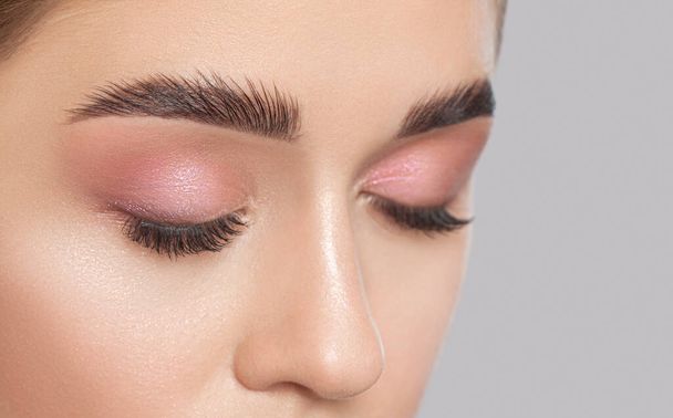 Beautiful young woman with long eyelashes, beautiful fresh nude make-up, thick eyebrows and with clean skin in a beauty salon. Eyelash extensions. Eyebrows close up. Make-up concept. - Photo, Image