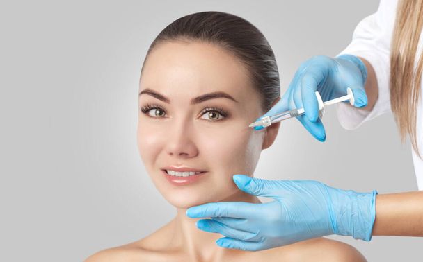 The doctor cosmetologist makes the Rejuvenating injections procedure for tightening and smoothing wrinkles on the face skin of a beautiful woman in a beauty salon.Cosmetology skin care. - Photo, Image