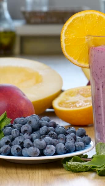Πεπόνι, βατόμουρο και smoothie βατόμουρο σε ένα ποτήρι στο φόντο των νωπών φρούτων και των μούρων. Το κοκτέιλ φρούτων είναι έτοιμο να φάει. Υγιεινή και χορτοφαγική έννοια των τροφίμων, Γκρο πλαν, κάθετη πλάνα - Πλάνα, βίντεο