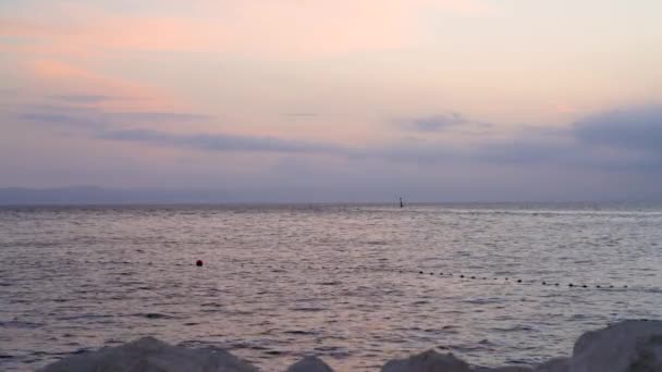 Geweldige zonsondergang op zee. Op de voorgrond staan stenen op de oever. Zwevende boei in de zee. Berglandschap aan de horizon. Kroatië - Video