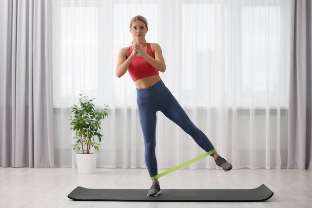 Athletic woman doing exercise with fitness elastic band on mat at home - Foto, imagen