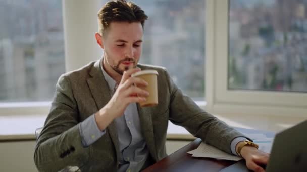 Busy handsome manager drinking coffee at office work on modern workplace close up. Focused business man enjoy beverage doing officework. Bearded company worker in glasses looking at laptop screen - Footage, Video