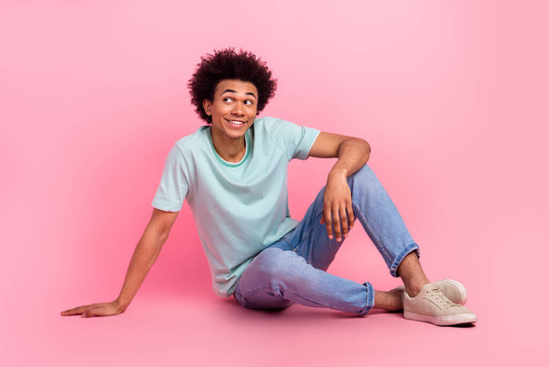 Foto de cuerpo completo de atractivo joven sentado piso posando mirada espacio vacío desgaste ropa azul de moda aislado sobre fondo de color rosa. - Foto, imagen