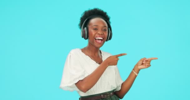 Pointing, music and black woman with headphones, happy and dance in studio isolated on a blue background mockup space. Radio, streaming and person hearing promotion, advertising and face portrait. - Footage, Video