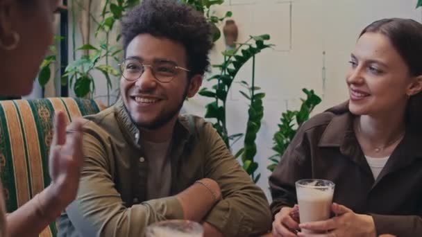 Közepes közelkép különböző fiatal férfi és női diákokról, akik együtt lógnak a kávézóban, élvezik a kávét, beszélgetnek, viccelődnek, vicces történeteket mesélnek és nevetnek - Felvétel, videó