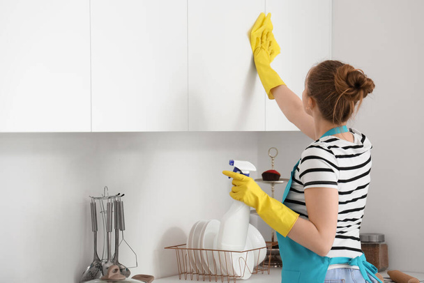 Mujer en guantes de goma amarilla limpiando armarios en cocina moderna - Foto, Imagen