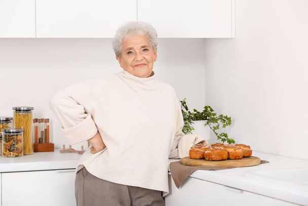 Ανώτερη γυναίκα με νόστιμα ψωμάκια στην κουζίνα - Φωτογραφία, εικόνα