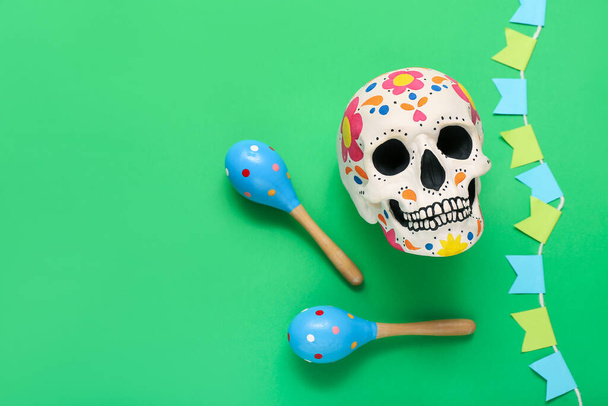 Painted human skull for Mexico's Day of the Dead (El Dia de Muertos) with maracas and garland on green background - Photo, Image
