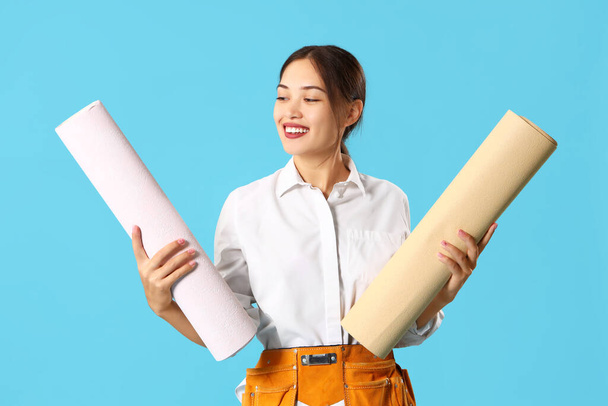 Female Asian decorator with wallpaper rolls on blue background - Photo, Image