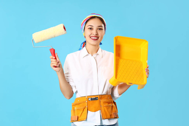 Female Asian decorator with paint roller and tray on blue background - Photo, Image