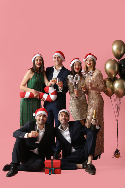 Группа молодых людей в шляпах Санта-Клауса с рисунком 2024 и шампанским на розовом фоне. Новогодний праздник - Фото, изображение
