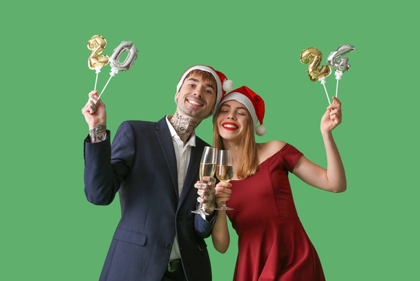 Jeune couple en chapeaux de Père Noël avec champagne et figure 2024 sur fond vert. Fête du Nouvel An - Photo, image