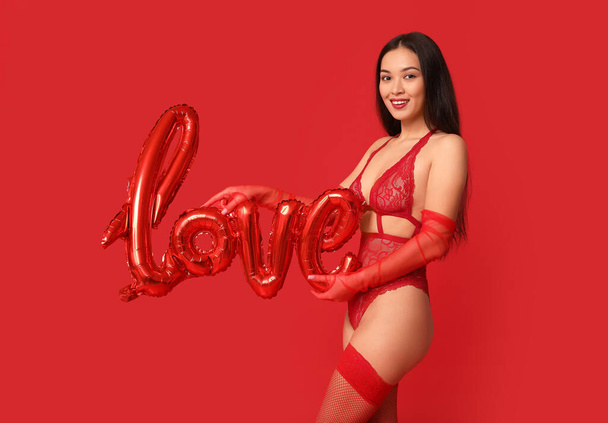 Όμορφη νεαρή σέξι Ασιάτισσα γυναίκα με μπαλόνι σε σχήμα λέξης ΑΓΑΠΗ σε κόκκινο φόντο. Γιορτή του Αγίου Βαλεντίνου - Φωτογραφία, εικόνα
