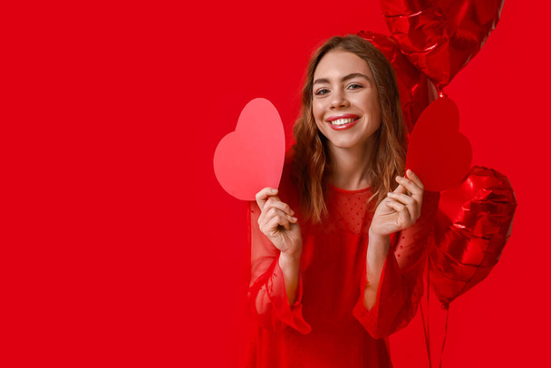 Kırmızı arka planda kağıt kalpleri ve balonları olan güzel genç bir kadın. Sevgililer Günü kutlaması - Fotoğraf, Görsel