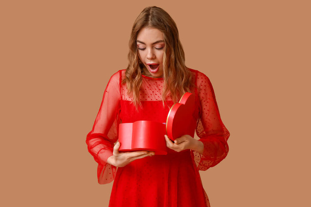 Verrast jonge vrouw openen geschenkdoos op bruine achtergrond. Valentijnsdag - Foto, afbeelding