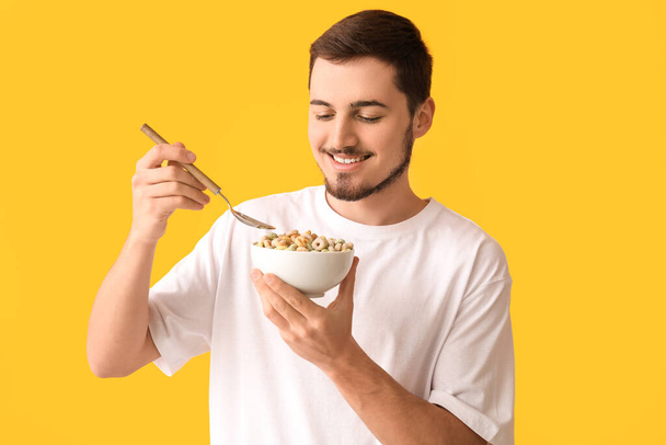 Handsome young man eating tasty cereal rings on yellow background - Photo, Image