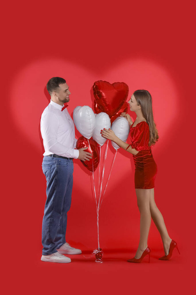 Schönes Paar mit Luftballons und herzförmigem Schatten auf rotem Hintergrund. Valentinstag-Feier - Foto, Bild