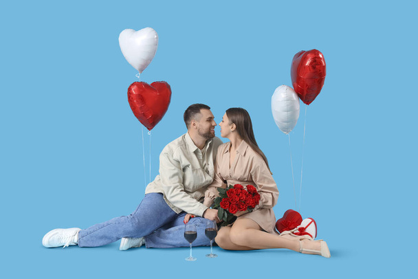 Krásný pár s sklenicemi vína, růží a balónky ve tvaru srdce na modrém pozadí. Valentýnská oslava - Fotografie, Obrázek