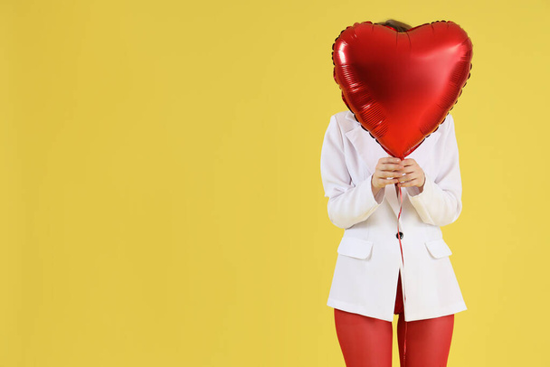 Young woman with heart shaped air balloon on yellow background. Valentine's Day celebration - Photo, Image